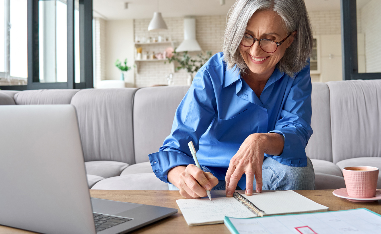 Smiling Elderly Woman Taking Down Notes from a Zoom Meeting